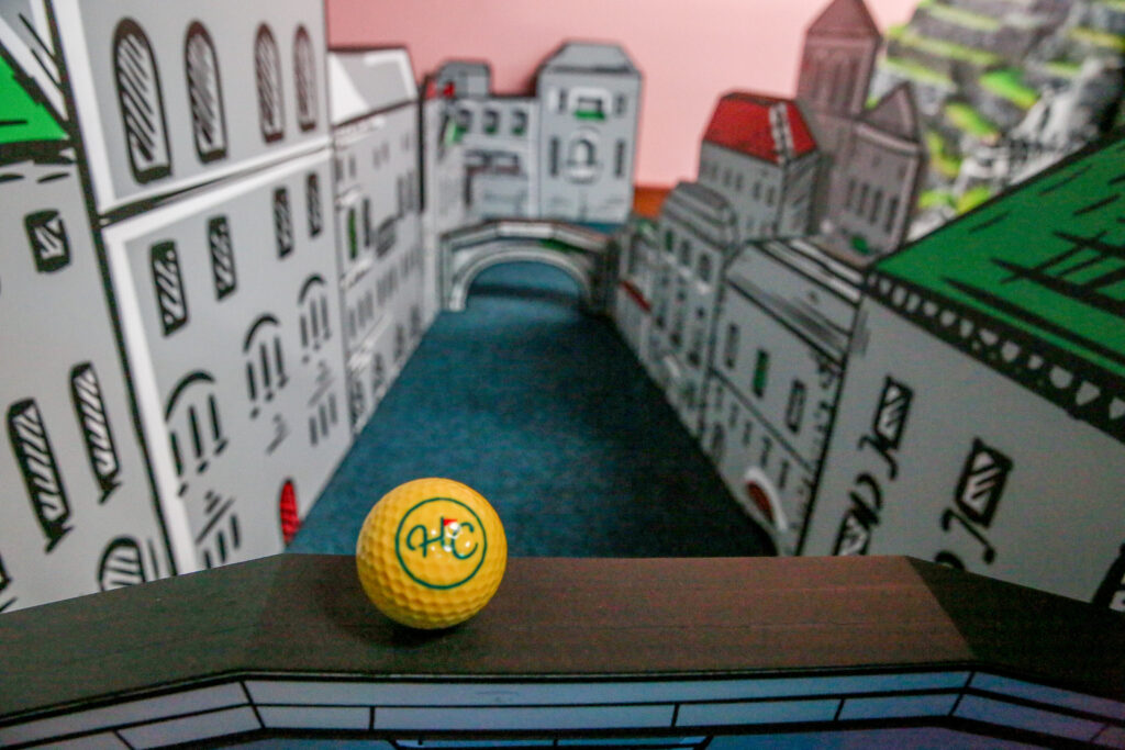 Mini golf hole with city bridge design and yellow golf ball at Hey Caddy