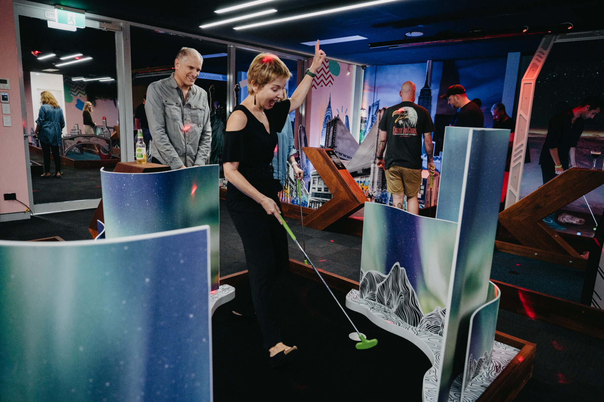 Woman celebrating while playing mini golf indoors with friends at Hey Caddy venue
