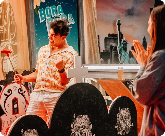 A man celebrating a winning putt on a themed indoor mini golf course at Hey Caddy, featuring Bora Bora and New York City obstacles, while a friend claps.