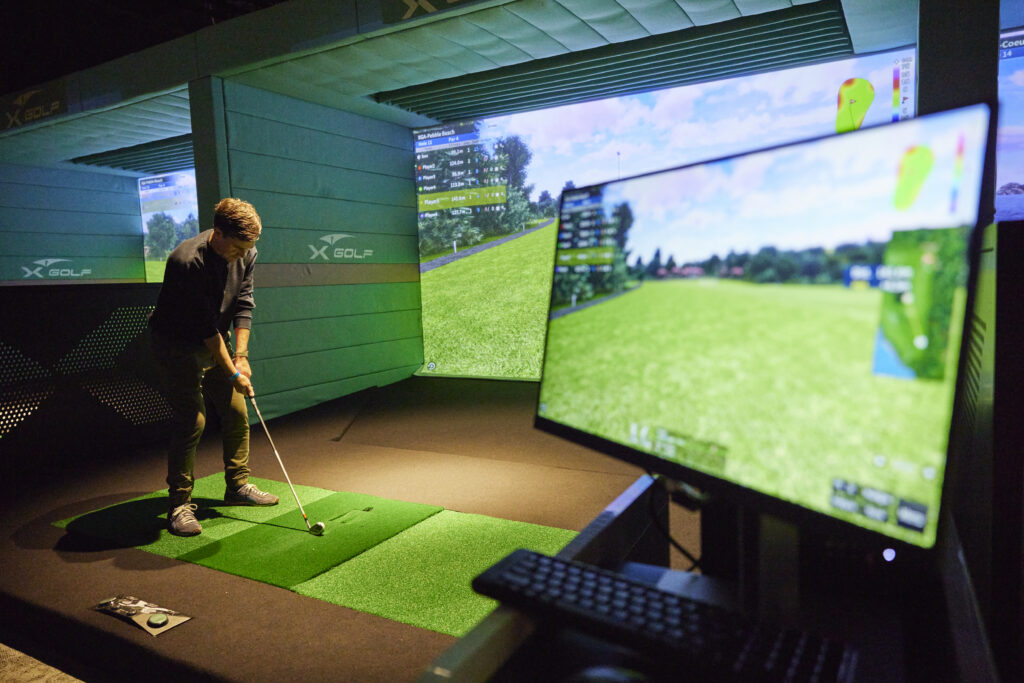 Man playing indoor golf simulator at X-Golf venue