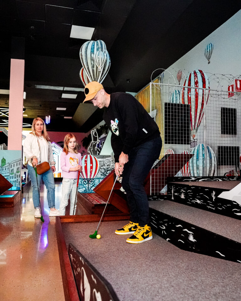 Man, Woman and Girl playing mini golf at Hey Caddy venue
