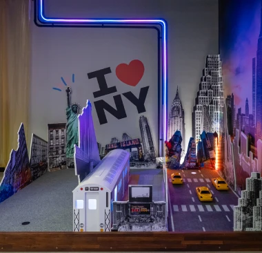 Hey Caddy New York themed mini golf hole featuring an I Love NY wall mural, subway car, Statue of Liberty cutout, and neon lights