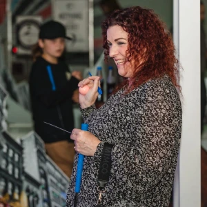 A smiling red-haired woman holding a blue golf putter and cheering after sinking a shot on a NYC-themed mini golf course at Hey Caddy.