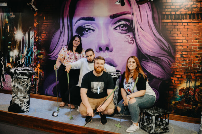 Friends posing with putters on a themed mini golf course in Macarthur