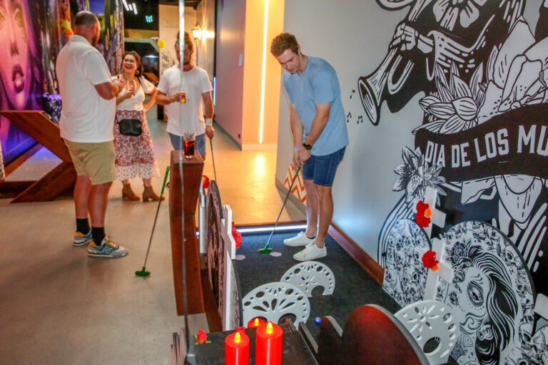 Player putting on a themed indoor mini golf course at Hey Caddy Palmerston