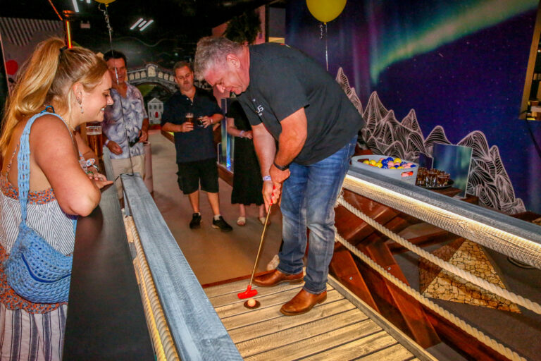 Adults playing indoor mini golf together at Hey Caddy Palmerston