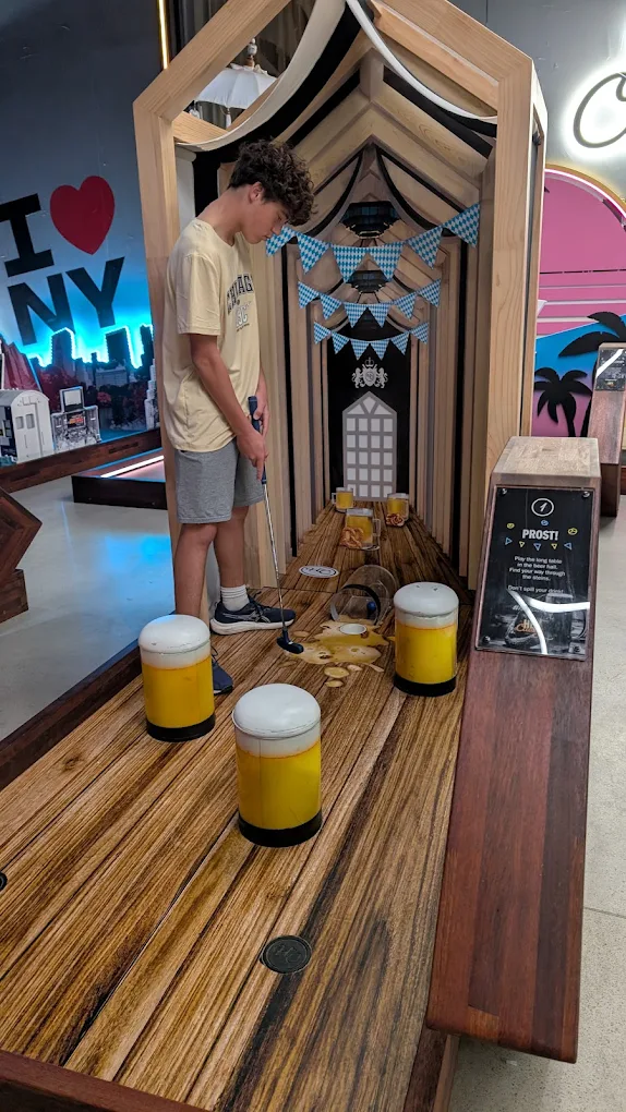 Player putting through a pub-themed indoor mini golf hole with oversized beer obstacles at Hey Caddy North Lakes
