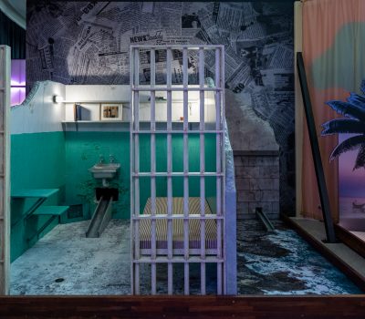 Prison themed mini golf hole with jail bars and urban backdrop at Hey Caddy