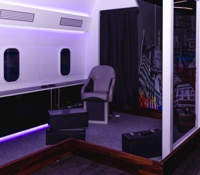 Airplane themed mini golf room with seats and cabin interior at Hey Caddy