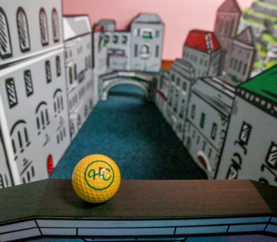 Mini golf hole with city bridge design and yellow golf ball at Hey Caddy