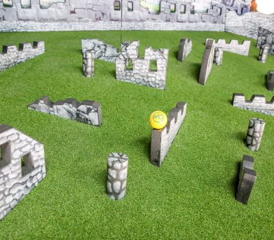 Mini golf course with stone ruins obstacles and yellow golf ball at Hey Caddy