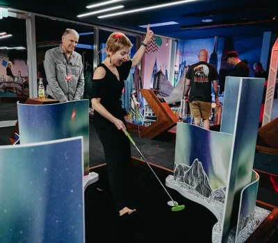 Guests playing mini golf at Hey Caddy under neon lights and city-themed backdrops