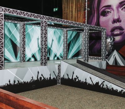 Concert themed mini golf hole with stage lighting and crowd silhouettes at Hey Caddy